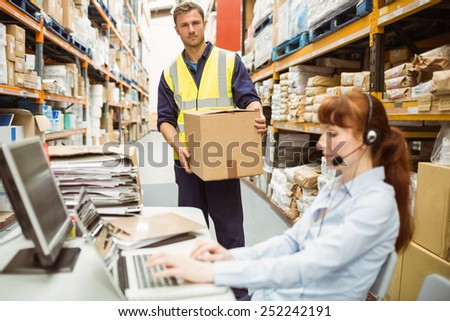 Warehouse manager wearing headset using laptop in a large warehouse