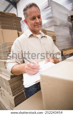 Warehouse worker checking his list on clipboard in a large warehouse