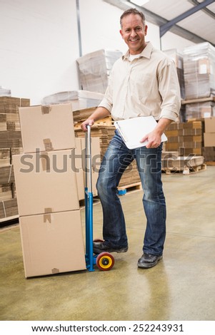 Delivery man leaning on trolley of boxes in a large warehouse