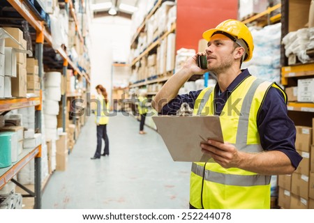 Warehouse worker talking on the phone holding clipboard in a large warehouse