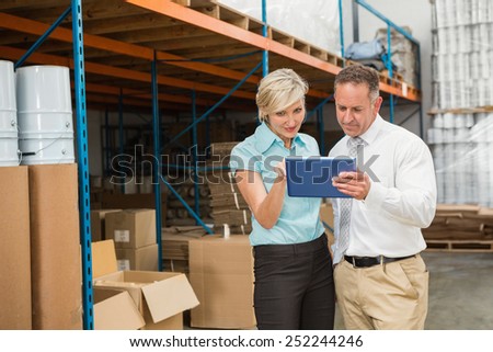 Warehouse managers looking at tablet pc in a large warehouse