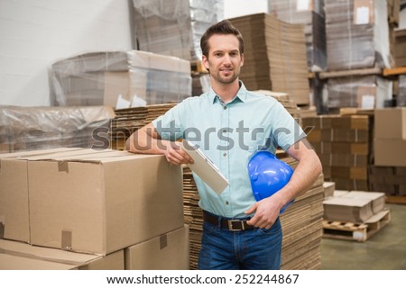 Smiling warehouse worker leaning against boxes in a large warehouse