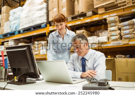 Warehouse management talking and looking at laptop in a large warehouse