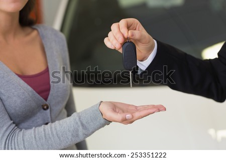 Smiling businessman giving car key to happy customer at new car showroom