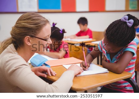 Cute pupil getting help from teacher in classroom at the elementary school