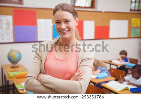 Pretty teacher smiling at camera with arms crossed at the elementary school