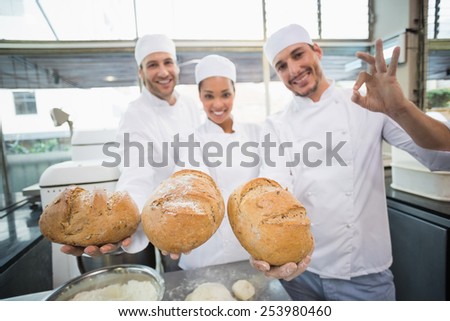 Team of bakers smiling at camera holding bread in the kitchen of the bakery