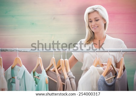 Pretty blonde looking through clothes rail against pink and green planks