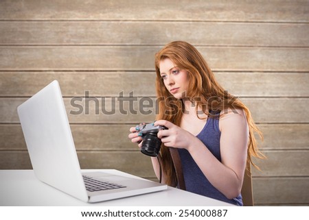 Pretty redhead working on laptop and camera against wooden surface with planks