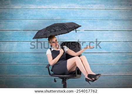 Businesswoman holding umbrella sitting on swivel chair against wooden planks