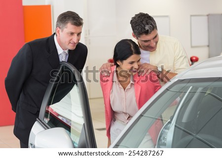 Car dealer showing the interior of a car to a couple at new car showroom