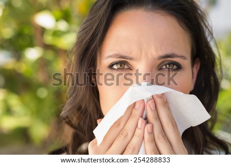 Pretty brunette blowing her nose on a sunny day
