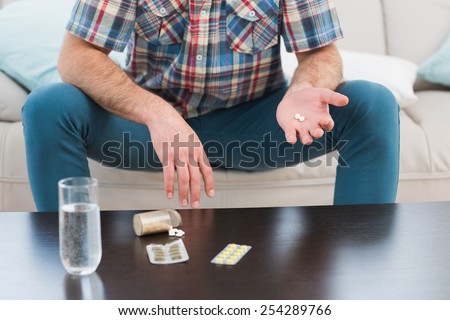 Man sitting on sofa holding pills at home in the living room
