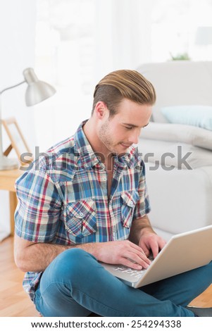 Smiling man sitting on the floor using laptop at home in the living room