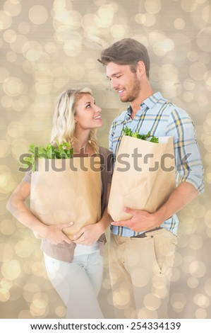 Attractive couple holding their grocery bags against light glowing dots design pattern