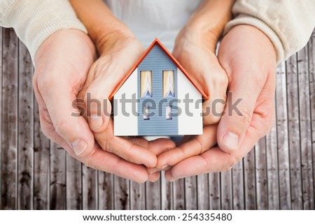 Couple holding small model house in hands against wooden planks