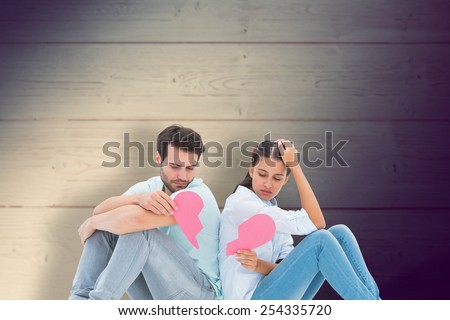Sad couple sitting holding two halves of broken heart against shadow on wooden boards