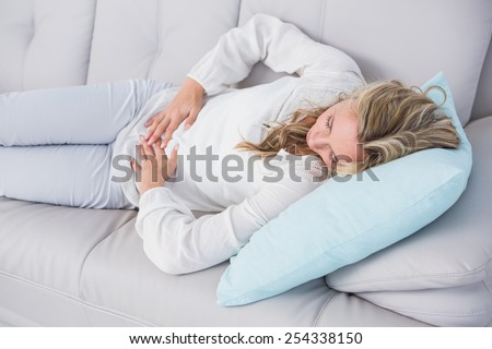 Blonde lying on couch getting stomach pain at home in the living room
