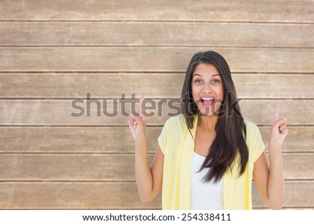 Happy casual woman pointing up against wooden surface with planks
