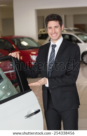 Smiling businessman showing a car for sale at new car showroom