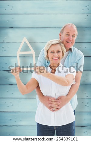 Happy older couple holding house shape against wooden planks