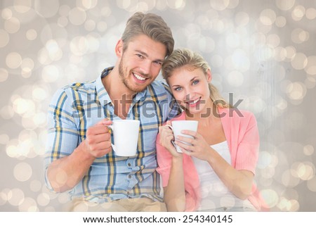 Attractive young couple sitting holding mugs against light glowing dots design pattern
