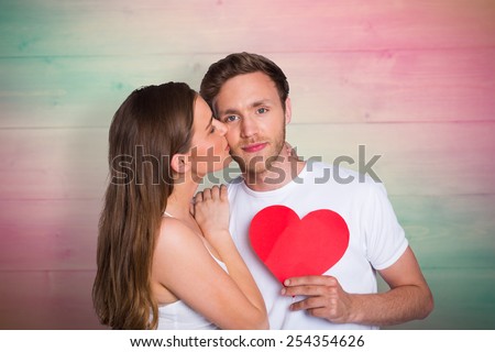 Woman kissing man as he holds heart against pink and green planks