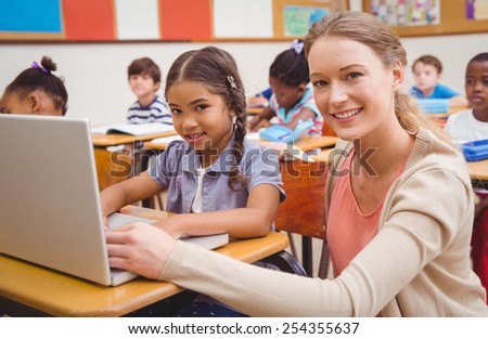 Cute pupil using computer with teacher at the elementary school