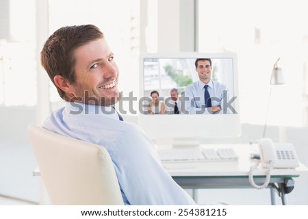 Cheerful businessman posing while his colleagues are working against smiling businessman sitting at his desk