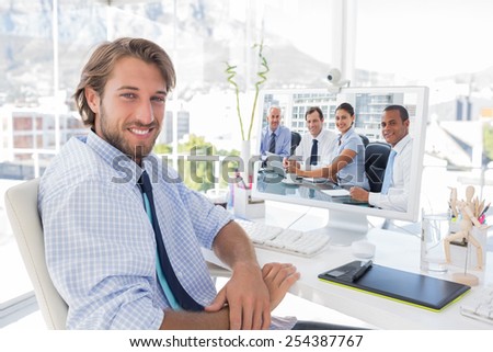 Business people brainstorming against smiling designer sitting at his desk