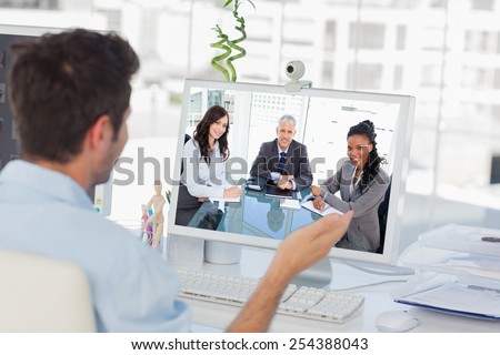 Smiling director sitting at the desk in front of the window between two employees against designer having a video chat