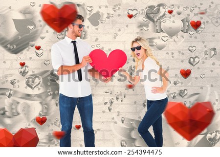 Cool young couple holding red heart against grey valentines heart pattern