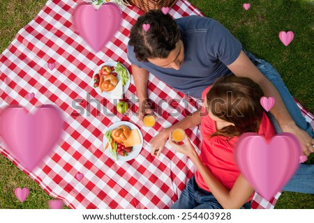 Elevated view of two friends lying on a blanket with a picnic against hearts