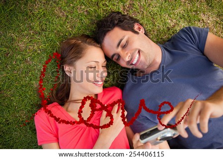 Two smiling friends looking at photos on a camera against love spelled out in petals