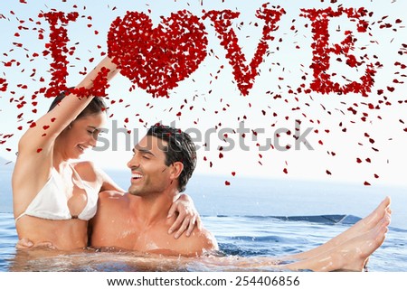 Happy couple enjoying time together in the pool against love spelled out in petals