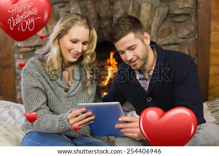 Couple using tablet PC in front of lit fireplace against cute valentines message