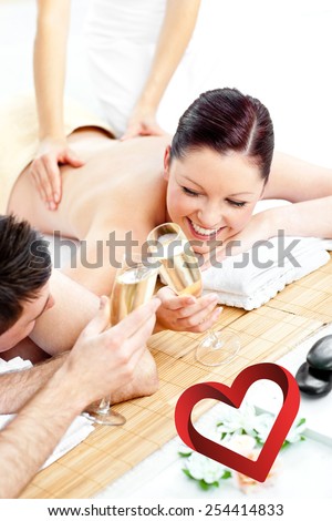 Loving young couple drinking champagne lying on a massage table against heart