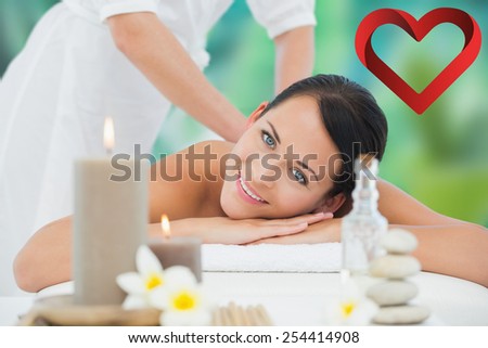 Beautiful brunette enjoying a back massage smiling at camera against heart