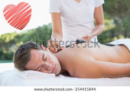 Handsome man getting a hot stone massage poolside against red heart