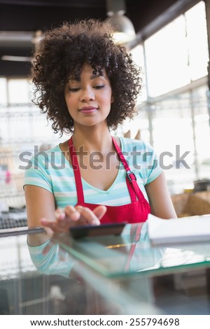 Pretty employee in red apron using calculator at the bakery