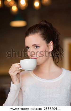 Pretty brunette sipping cup of coffee at the cafe