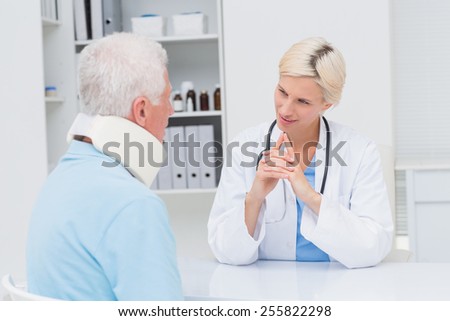 Female doctor looking at senior patient wearing neck brace in clinic