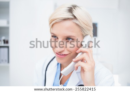 Confident female doctor using telephone while looking away in clinic