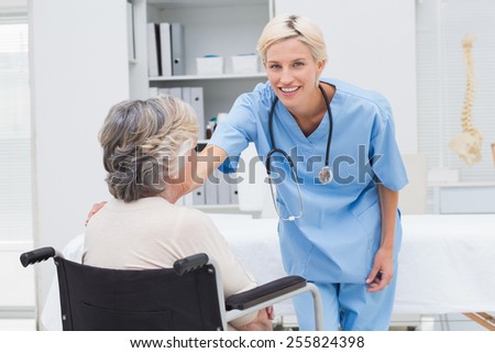 Portrait of happy female nurse consoling patient sitting on wheelchair in clinic
