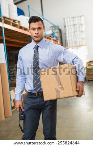 Warehouse manager holding cardboard box and scanner in a large warehouse
