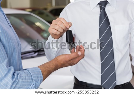 Businessman giving car key to customer at new car showroom