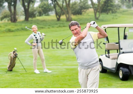 Golfer about to tee off with partner behind him on a foggy day at the golf course