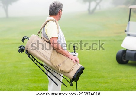 Happy golfer with golf buggy behind on a foggy day at the golf course