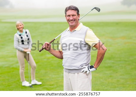 Happy golfer teeing off with partner behind him on a foggy day at the golf course