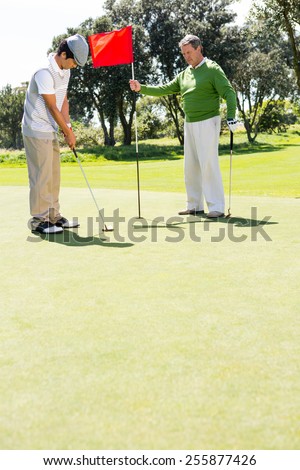 Golfer holding hole flag for friend putting ball at the golf course